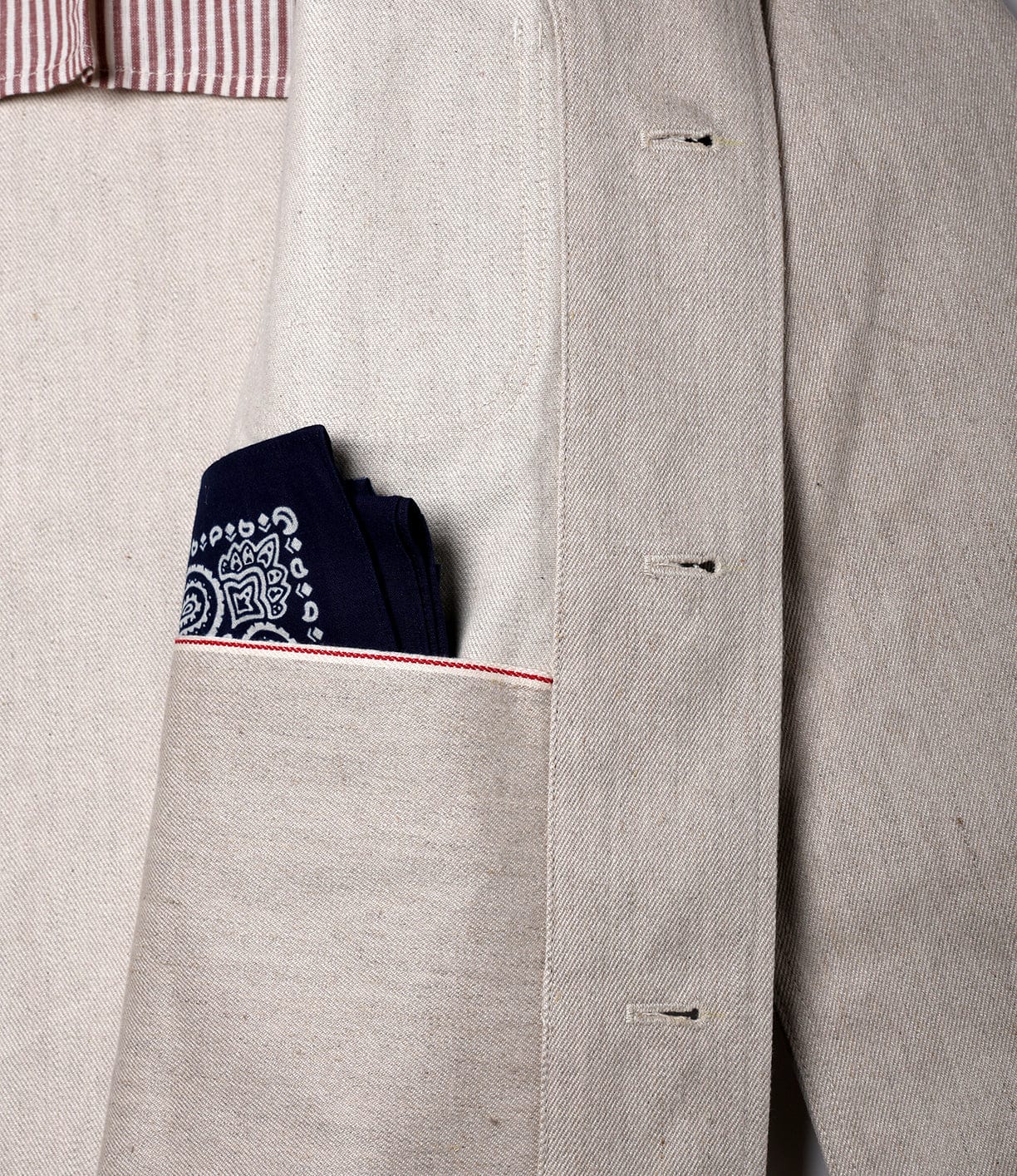 A close-up of the Selvedge Beige Studio Jacket by Best Made Co shows its beige pocket with a dark blue patterned pocket square, striped red and white lining, and unfinished buttonholes—details that reflect its American craftsmanship.