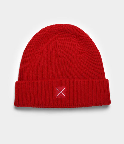 The Cap of Courage by Best Made Co. is a bright red lambswool cap with a folded brim and a small rectangular patch featuring a white X on the front center, shown on a plain light background.