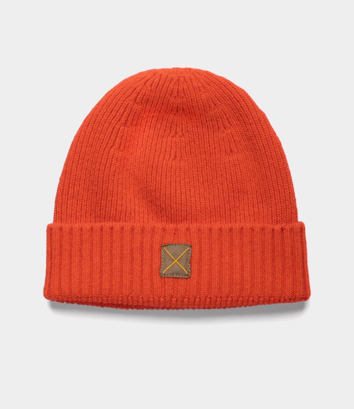 The Cap of Courage by Best Made Co is an orange knit lambswool cap with a folded brim and a small brown rectangular front patch, shown against a plain white background.