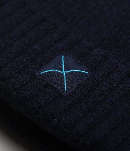 Close-up of the dark blue ribbed knit Cap of Courage by Best Made Co., featuring a small black patch with a light blue embroidered X.