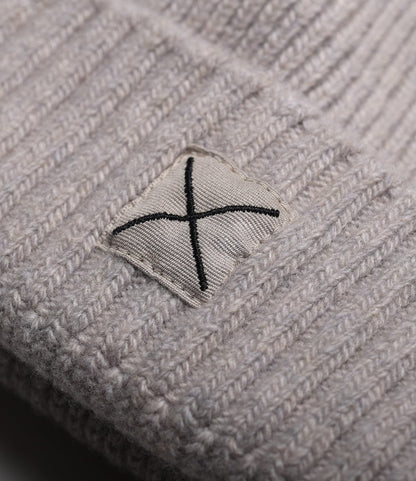 A close-up of the Cap of Courage by Best Made Co.—a light grey knitted lambswool beanie with a rectangular patch featuring a bold black X. The knit texture and patch details are clearly visible.