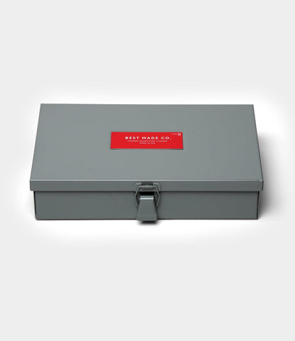 A closed, rectangular gray steel Type 9 Strongbox by Best Made Co., featuring a front latch and a red "Best Made Co." label on the lid, set against a plain white background.