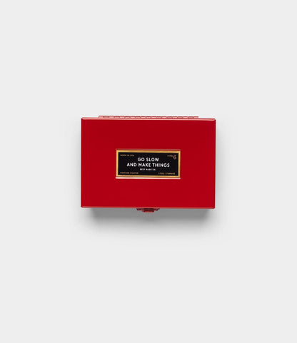 The Type 6 Strongbox, Go Slow Edition by Best Made Co. is a small red box with a black and gold front label reading "GO SLOW AND MAKE THINGS" in white capitals, shown on a plain light gray background.