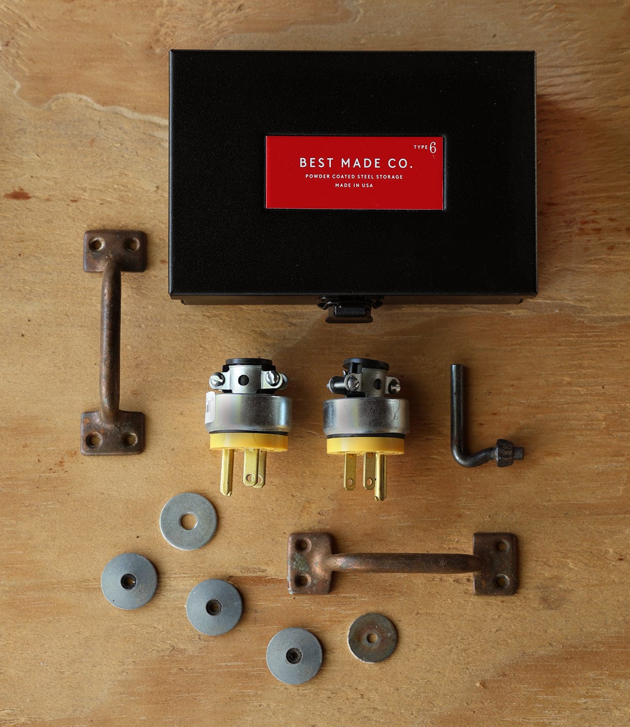 A durable steel Type 6 Strongbox, Go Slow Edition by Best Made Co. rests on a wooden surface amid hardware items—plugs, handles, an L-shaped hex key, and washers—showcasing one of Best Made Co’s iconic strongboxes.