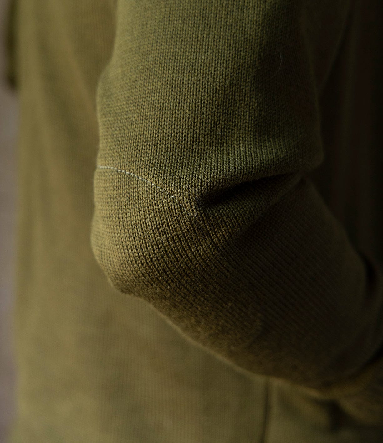 Close-up of the elbow area of a person wearing the Best Made Co. Dehen Shawl Neck Sweater in Moss Green, highlighting its textured worsted wool knit and stitching inspired by classic American workwear.