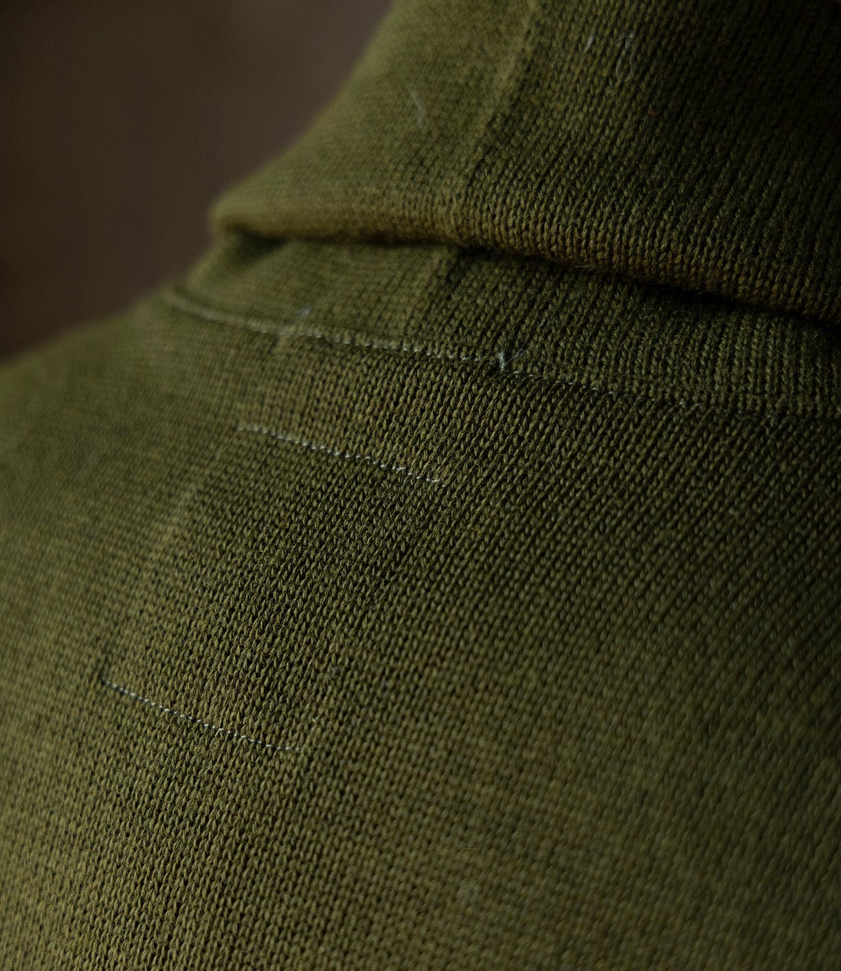 Close-up of the Dehen Shawl Neck Sweater in Moss Green by Best Made Co., featuring a visible rectangular patch repair that showcases the textured worsted wool and fine details inspired by classic American workwear.