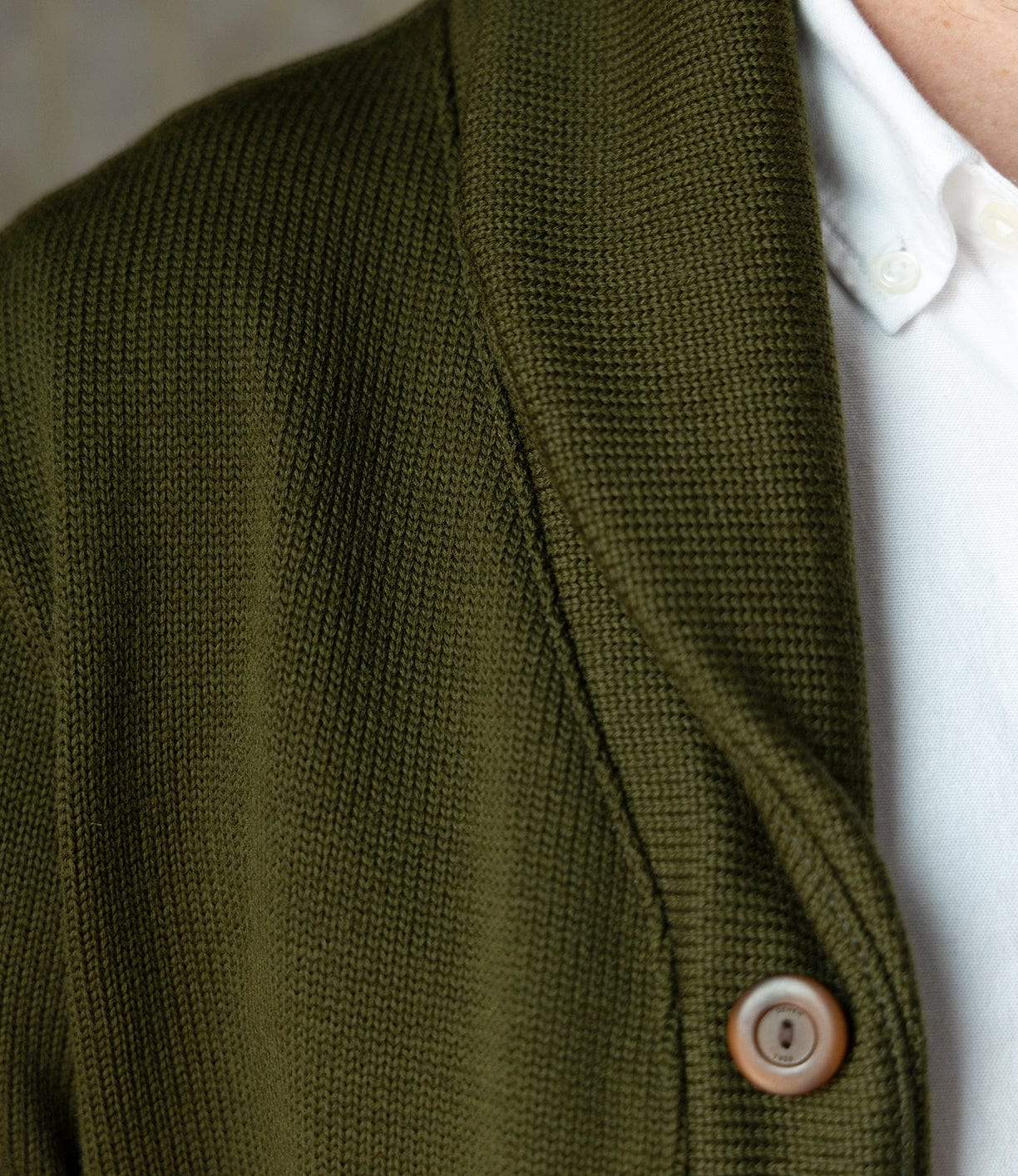 Close-up of a person wearing the Best Made Co. Dehen Shawl Neck Sweater in Moss Green over a white collared shirt. Only the shoulder and part of the chest are visible, evoking classic American workwear style.