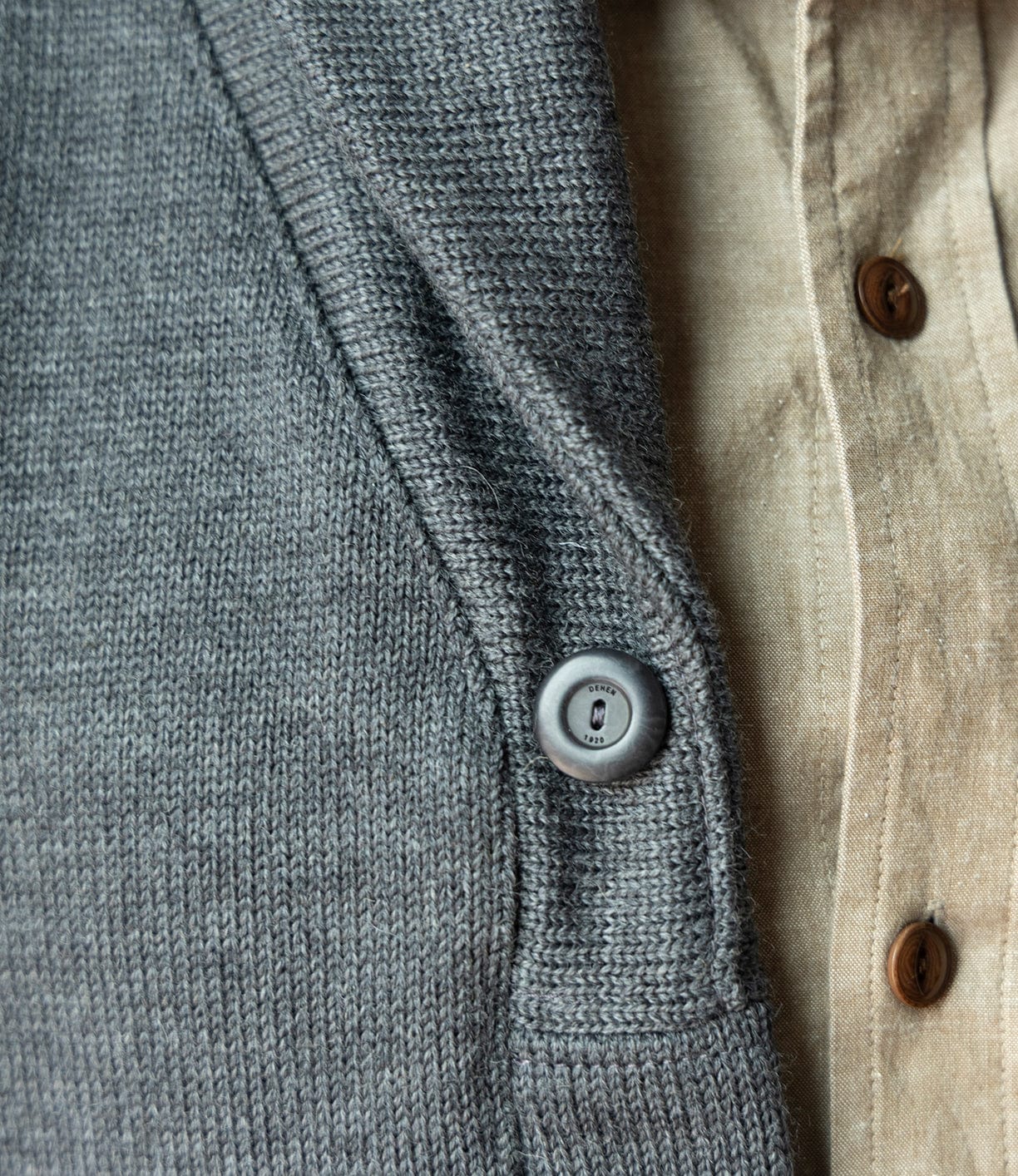 Close-up of the Dehen Shawl Neck Sweater in Charcoal by Best Made Co., a grey worsted wool knit cardigan with a dark button, layered over a beige shirt. The textures evoke classic American workwear and showcase quality materials.