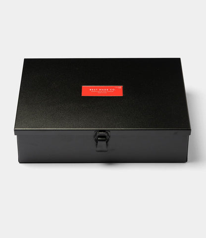 The Type 12 Strongbox - Matte Black by Best Made Co. is a durable steel box with a latch and a red lid label featuring the brand name in white. Ideal for secure storage, it's shown against a plain white background.