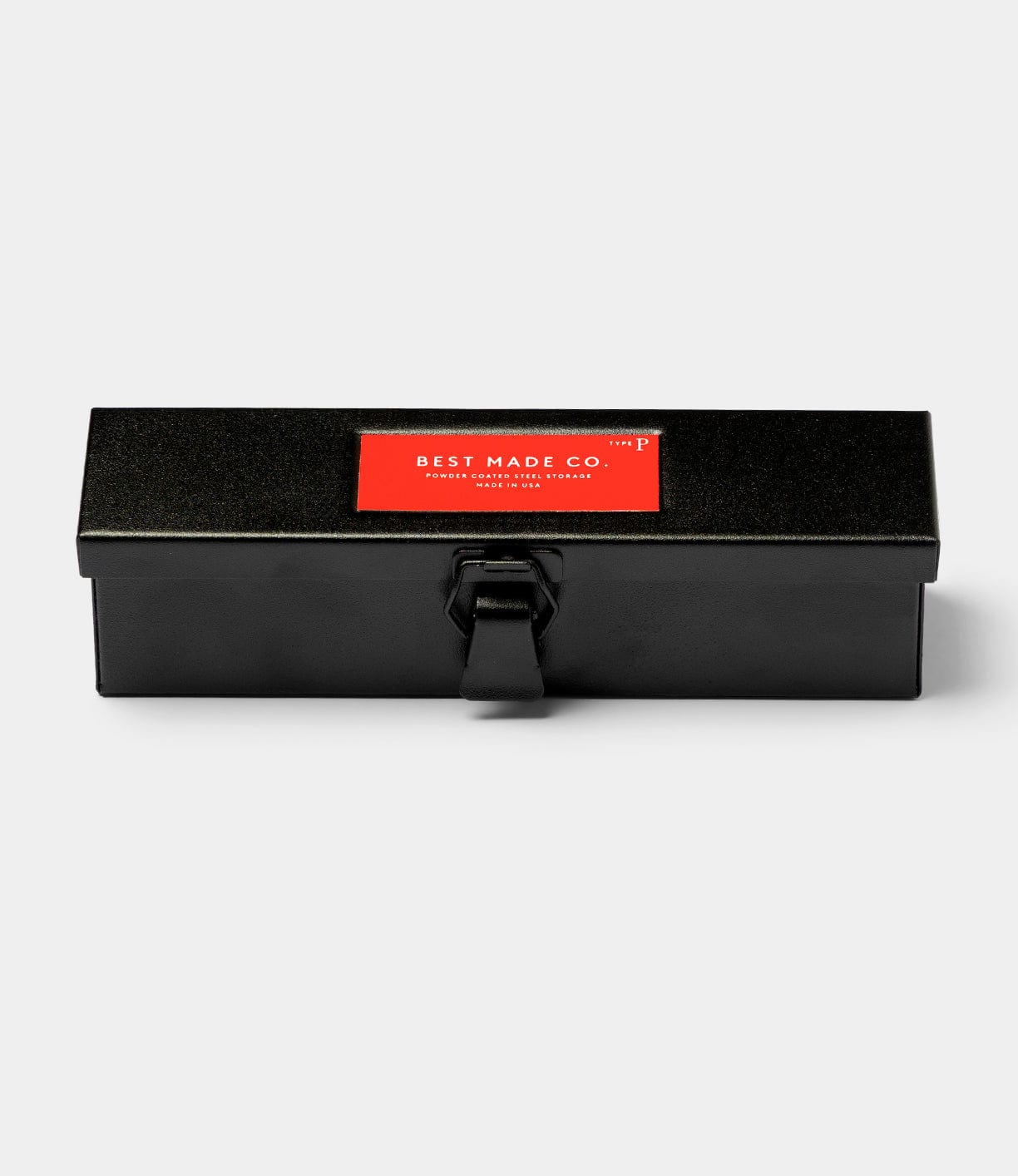 The Type P Strongbox, Go Slow Edition by Best Made Co is a rectangular black steel box with a front latch and a red label on top displaying the brand name in white, shown against a plain light gray background.