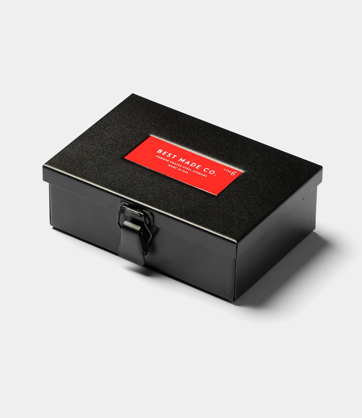 The Best Made Co Type 6 Strongbox, Go Slow Edition, is a durable black steel rectangular box with a latch closure and a red lid label reading "Best Made Co." in white, shown against a plain light gray background.