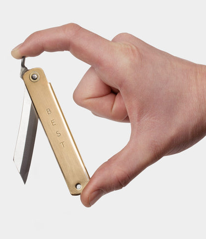 A hand holds the Max Brass Higo Knife by Best Made Co, highlighting the elegant and simple design of this handmade Japanese folding knife.