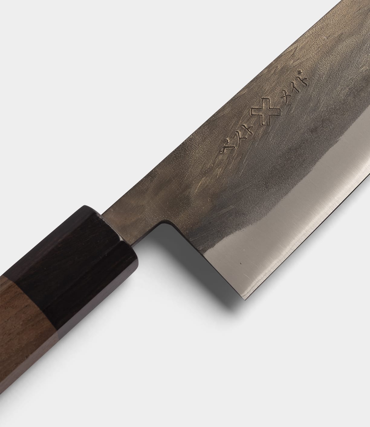 A close-up of the Best Made Co. Aogami Santoku Knife, showcasing its dark wooden handle and lustrous Blue Paper Steel blade adorned with engraved markings near the handle, set against a light background.