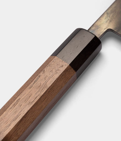 Close-up of the wooden handle of the Best Made Co. Aogami Gyuto Knife, featuring a dark bolster and highlighting the smooth texture and natural grain of the wood against a plain, light background. This elegant handle is designed for both comfort and precision, reflecting the quality craftsmanship of this Japanese chef knife.