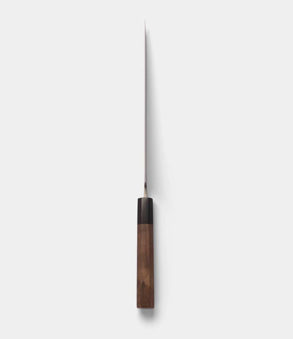 The Best Made Co. Aogami Gyuto Knife is displayed from above, highlighting its slender silver blade—made with Blue Paper Steel No. 2—and its rectangular wooden handle, which casts a narrow shadow on a simple light gray background.