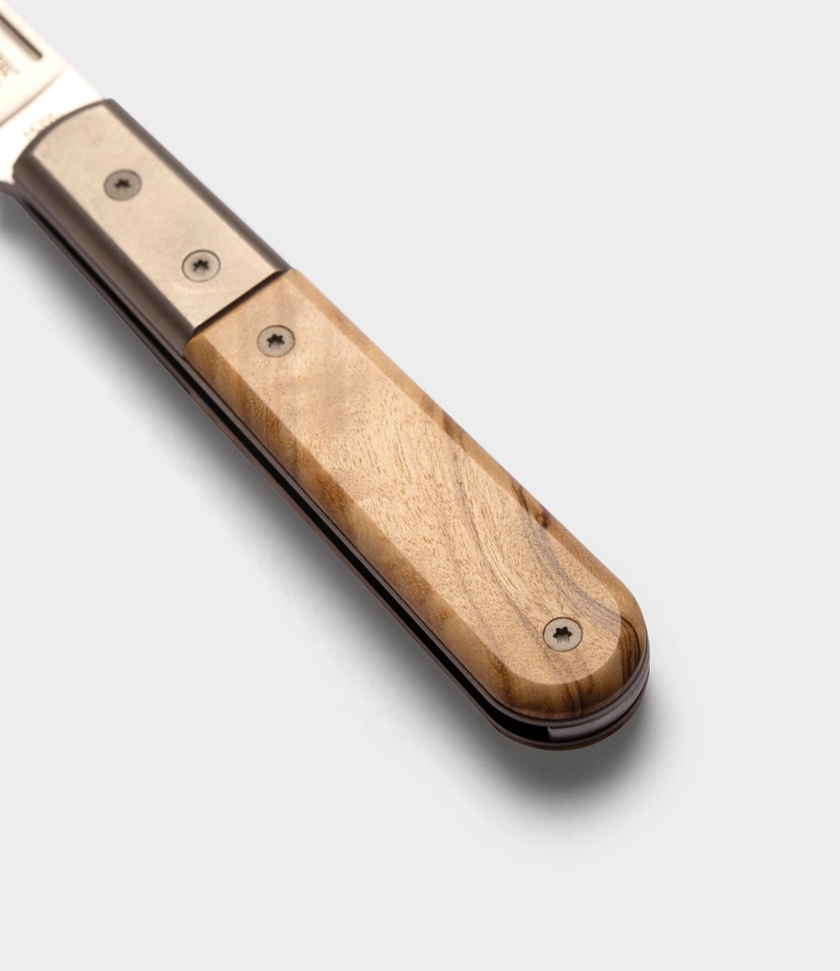 Close-up of a Best Made Co. Italian Barlow knife handle with polished wood and metal, visible screws on the wooden section, set against a plain light gray background.