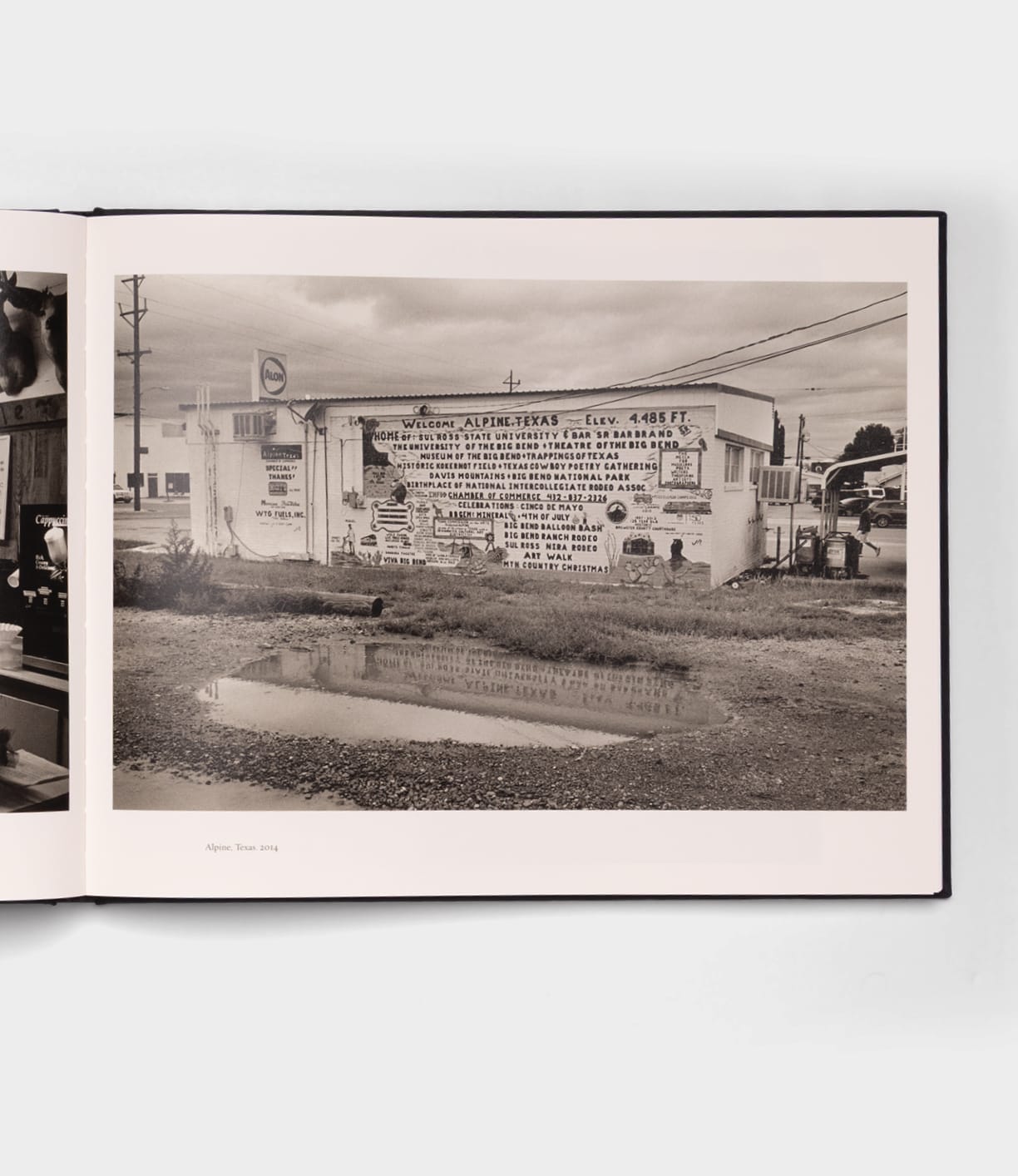 Open Range by Best Made Co.: a black-and-white photo of a building in Alpine, Texas, its mural mirrored in a puddle beneath a cloudy sky—capturing the quiet rural mood reminiscent of Robert Adams’ photography.