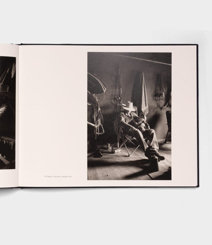 A black-and-white photo in Best Made Co.'s photography book "Open Range" depicts a person in a cowboy hat on a folding chair, surrounded by saddles and ranch equipment in dim light, evoking the quiet storytelling of Robert Adams.
