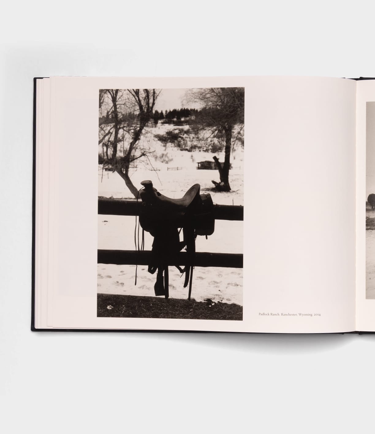 A black-and-white photo in the "Open Range" photography book by Best Made Co. shows a horse saddle hanging on a wooden fence before a snowy field and bare trees, evoking the timeless style of Robert Adams.