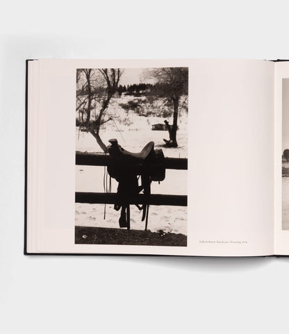 A black-and-white photo in the "Open Range" photography book by Best Made Co. shows a horse saddle hanging on a wooden fence before a snowy field and bare trees, evoking the timeless style of Robert Adams.