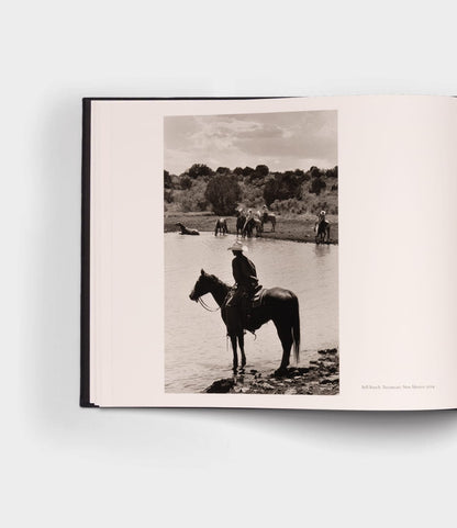 An open photography book, "Open Range" by Best Made Co., shows a black-and-white image of a rider on horseback near water, with other horses and riders in the background among sparse trees—evoking classic landscapes.