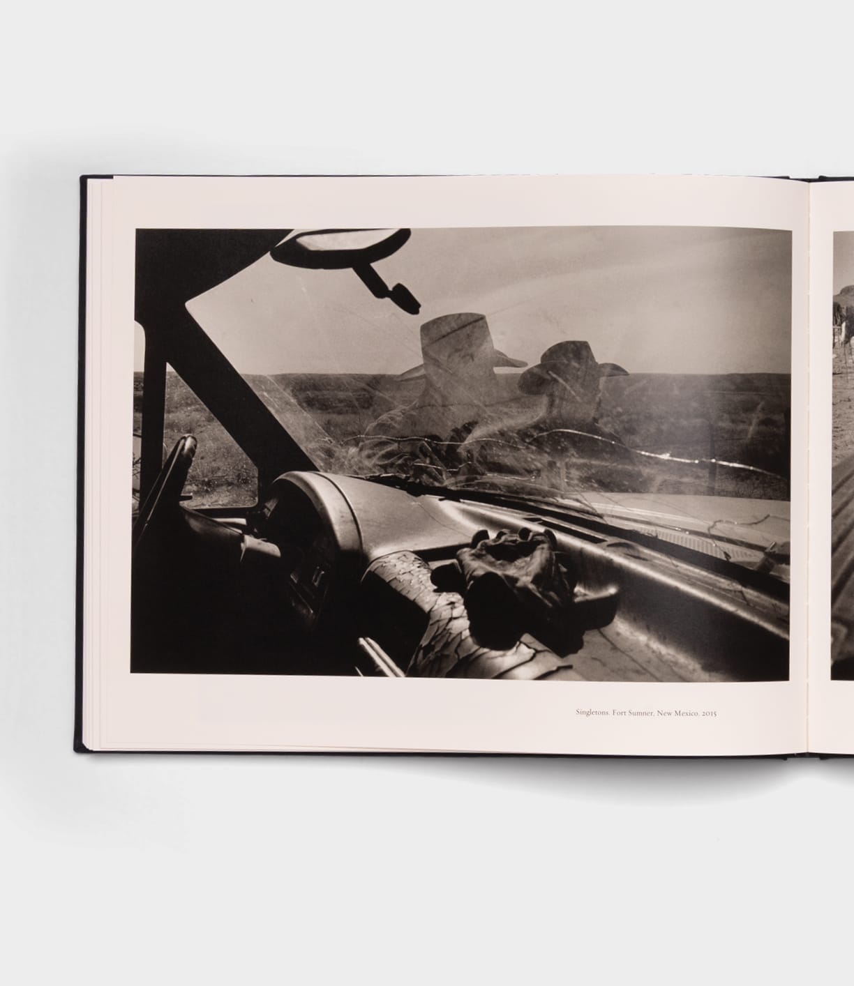 Black-and-white photo of a car interior with gloves on the dashboard and two figures outside, seen in an open copy of Open Range by Best Made Co.