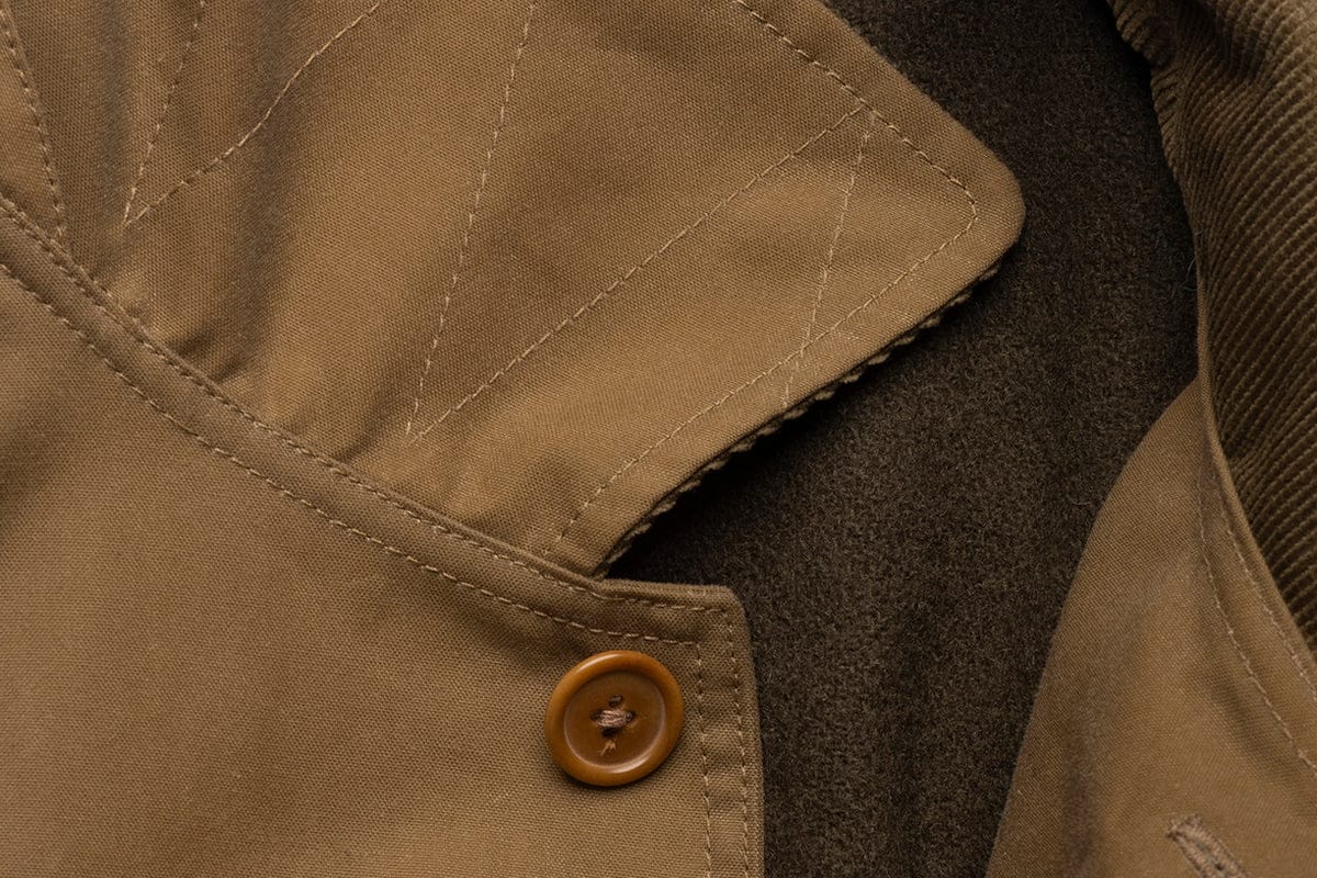 Close-up of a brown coat featuring a tan button, visible stitching, and a mix of smooth and textured fabric layers.