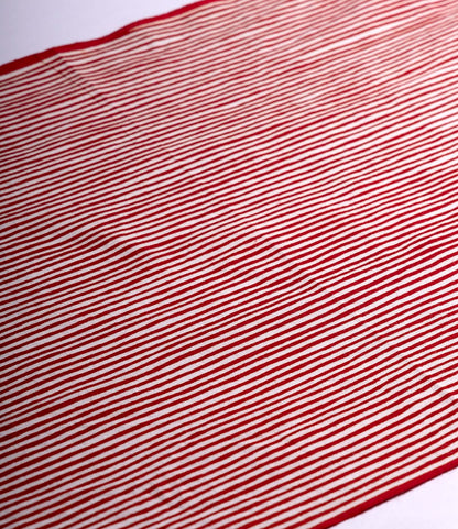 The Yoroke-Jima Tenugui by Best Made Co. features red and white horizontal stripes on hand-dyed Japanese fabric, laid flat with gentle wrinkles and shadows for a wabi-sabi feel. Evenly spaced stripes span the entire cloth.