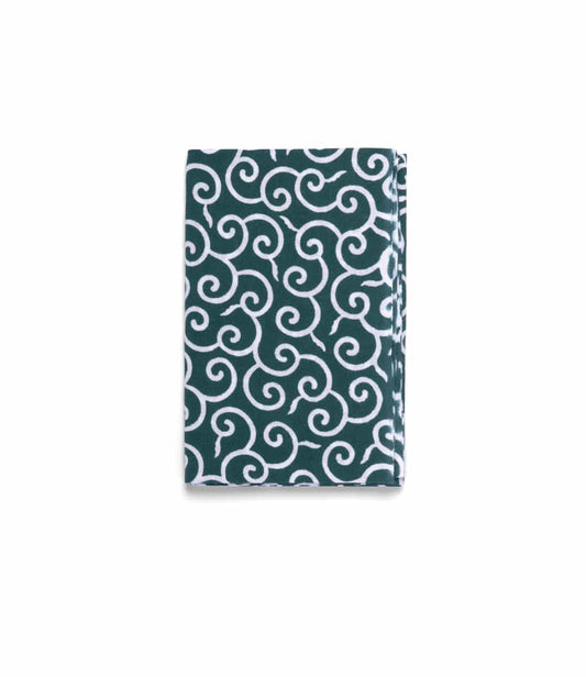 A folded Karakusa Tenugui by Best Made Co.—a hand-dyed Japanese cloth with a dark green background and intricate white swirling pattern—displayed on a plain light gray surface.