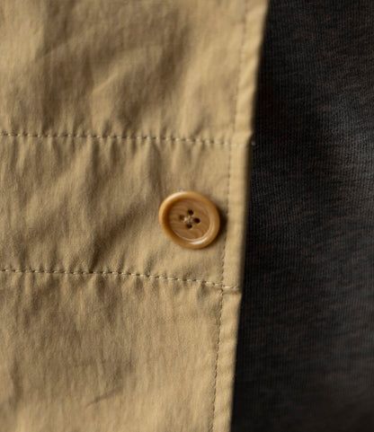 Close-up of a beige button on tan fabric, part of the Possibilities Jacket Tan by Best Made Co. Durable and lightweight, with dark gray or black Cordura ripstop jacket fabric visible on the right. Stitching and textures are sharply defined.