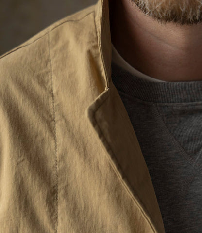 Close-up of a person wearing the Best Made Co. Possibilities Jacket Tan over a grey crew-neck sweatshirt, with part of their lower face and beard visible, highlighting the jacket's texture and layered look.