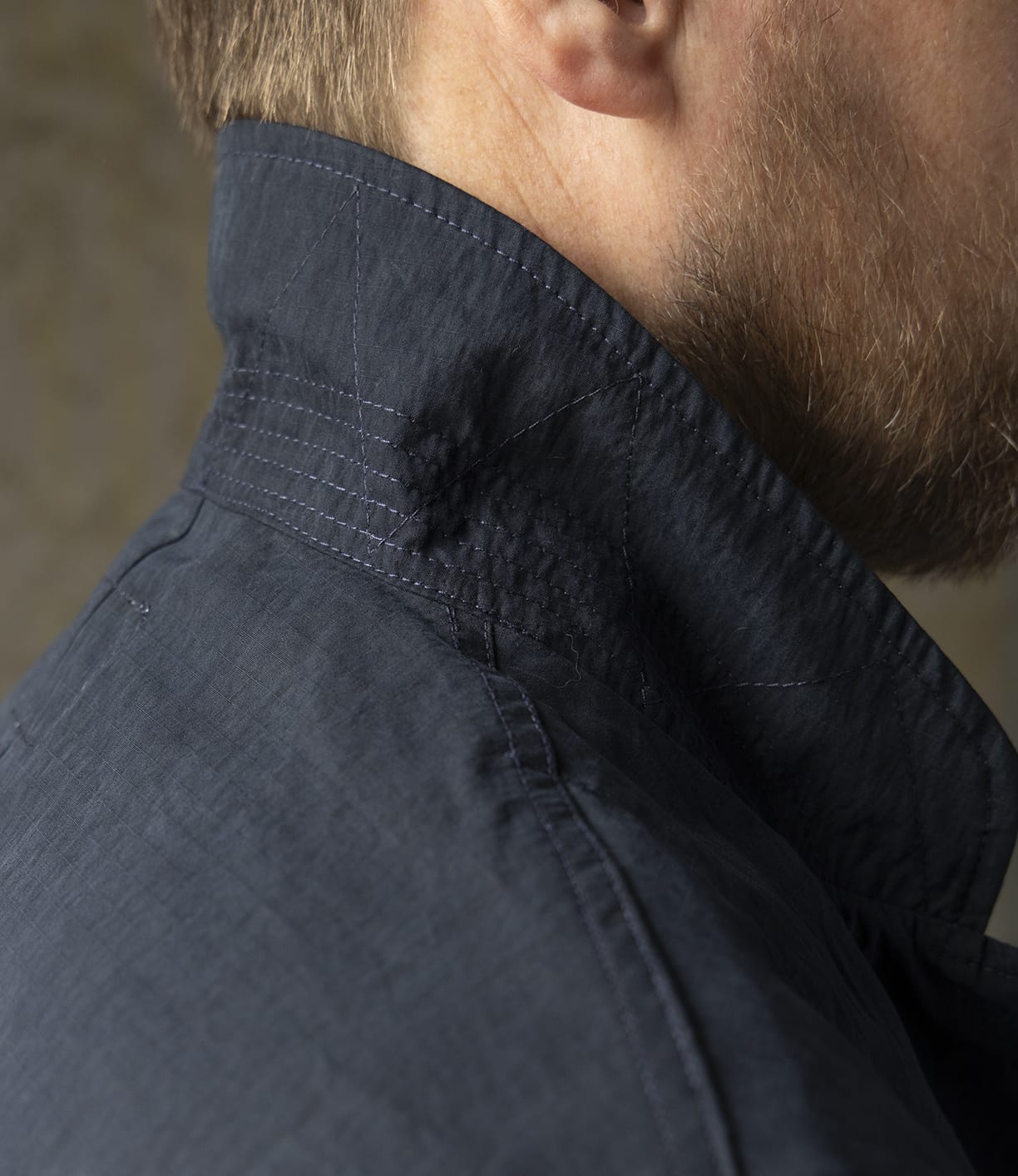 Close-up of a man's neck and jawline with a neatly trimmed beard, wearing the Best Made Co Possibilities Jacket Navy—crafted from organic cotton denim with visible stitching. The turned-up collar emphasizes American craftsmanship and rich texture.