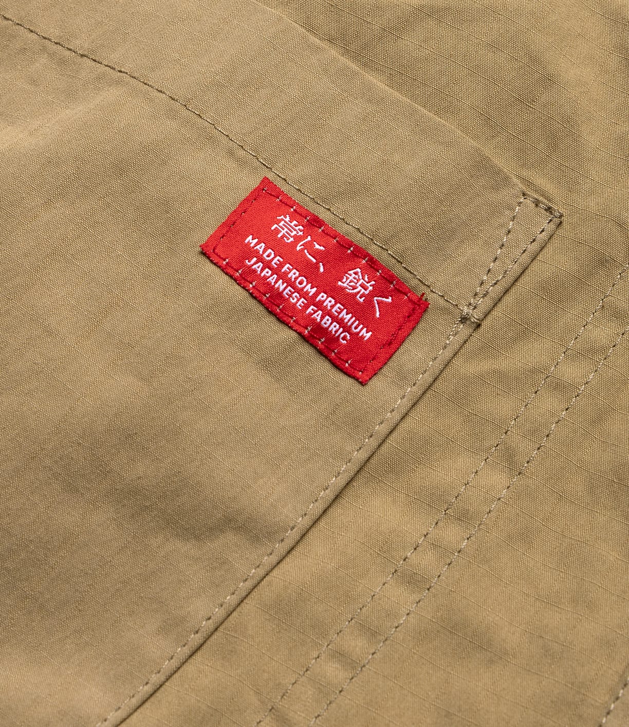 Close-up of tan fabric with visible stitching and a red tag reading MADE FROM PREMIUM JAPANESE FABRIC, highlighting Best Made Co's Possibilities Jacket Tan—crafted from organic cotton selvedge denim with American craftsmanship.