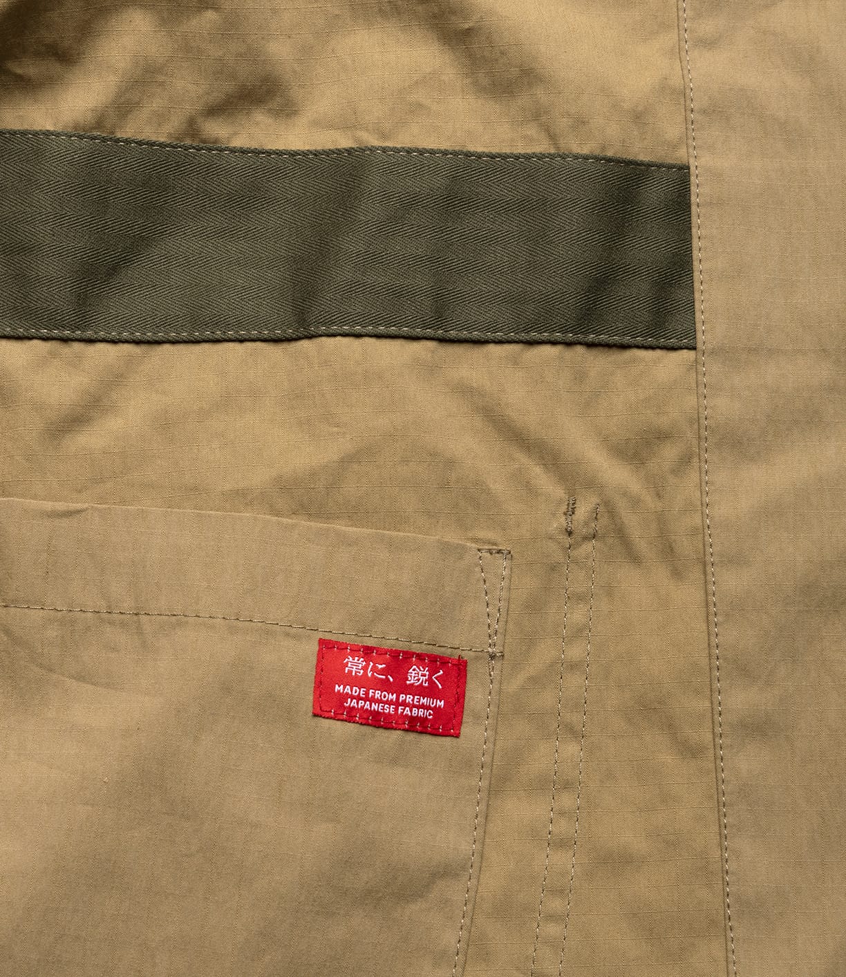A close-up of the Best Made Co Possibilities Jacket Tan shows organic cotton selvedge denim with a green stripe, a stitched pocket, and a red label reading, “MADE FROM PREMIUM JAPANESE FABRIC.”.