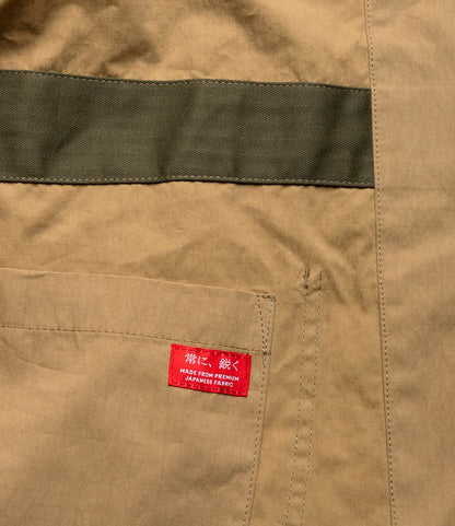 A close-up of the Possibilities Jacket Tan by Best Made Co.—khaki fabric with a green stripe, pocket, and red label in Japanese reading "Made from Premium Japanese Fabric," highlighting its durable, lightweight craftsmanship.