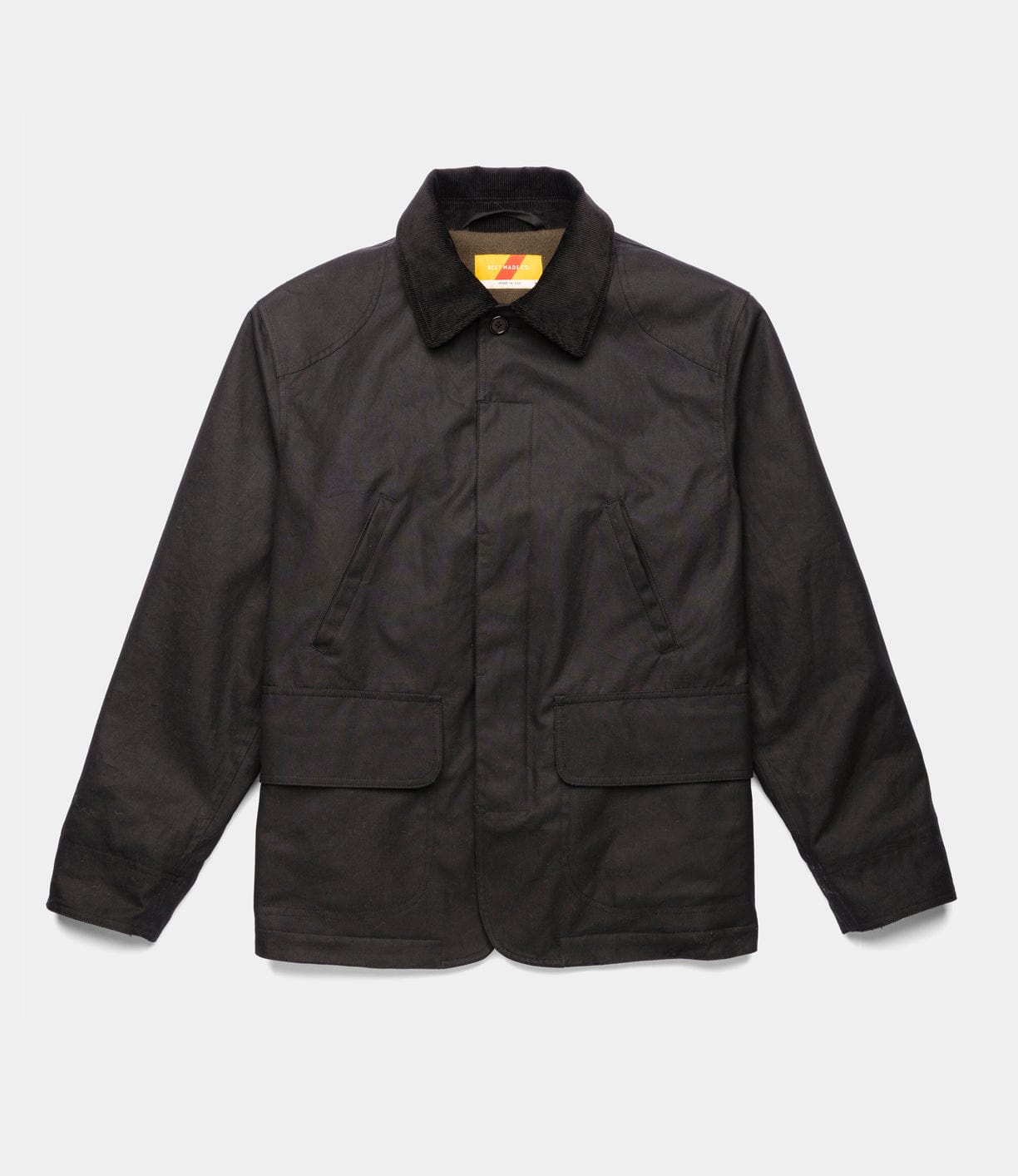 The Best Made Co. Wool-Lined Waxed Field Jacket Black features long sleeves, a collared button-up front, two angled chest pockets, and two waist flap pockets, shown against a plain white background.