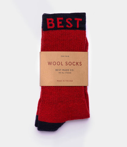 A pair of red and black Standard Wool Socks by Best Made Co., labeled BEST at the top, wrapped in a brown paper band reading “Wool Socks, Best Made Co., Made in the USA,” offering moisture-wicking all-season comfort against a plain white background.