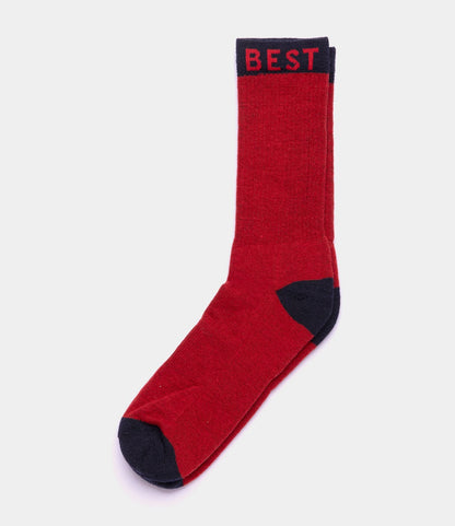 The Best Made Co. Standard Wool Sock, shown flat on a white background, is red with black toe, heel, and cuff details. "BEST" is written in red on the cuff. Designed for all-season comfort with soft merino wool.