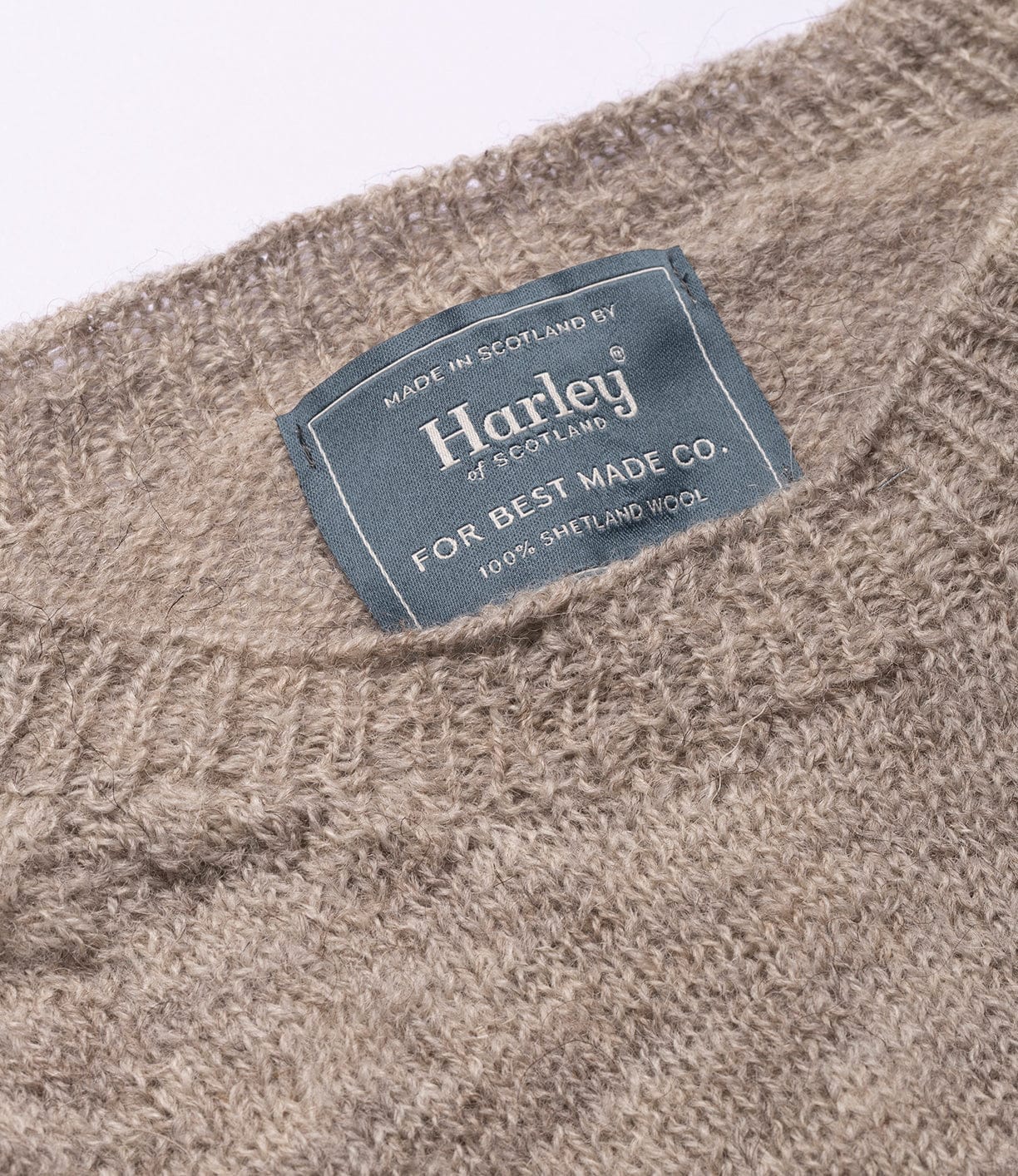 A close-up of the beige 5-Gauge Shetland Sweater by Best Made Co., crafted from 100% Shetland wool in Scotland with seamless construction, and featuring a blue "Harley of Scotland for Best Made Co." label. Lightweight and warm.