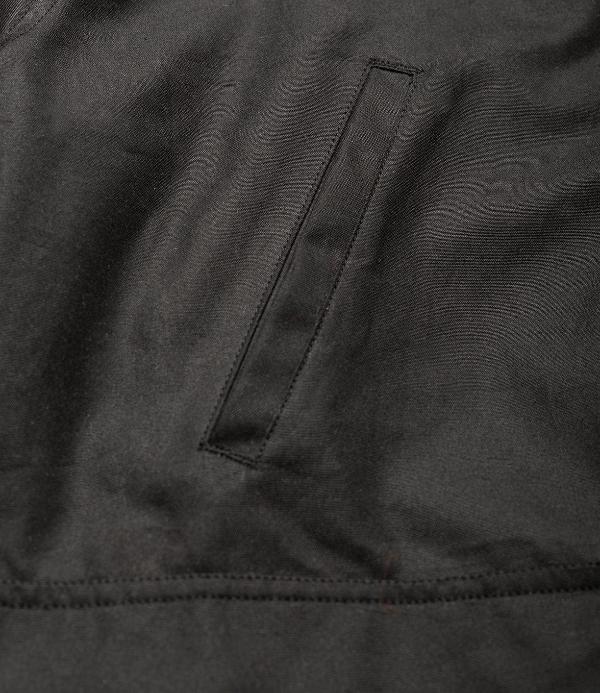 Close-up of the Best Made Co. Wool-Lined Waxed Field Jacket in black, featuring a single narrow horizontal welt pocket and visible stitching details.