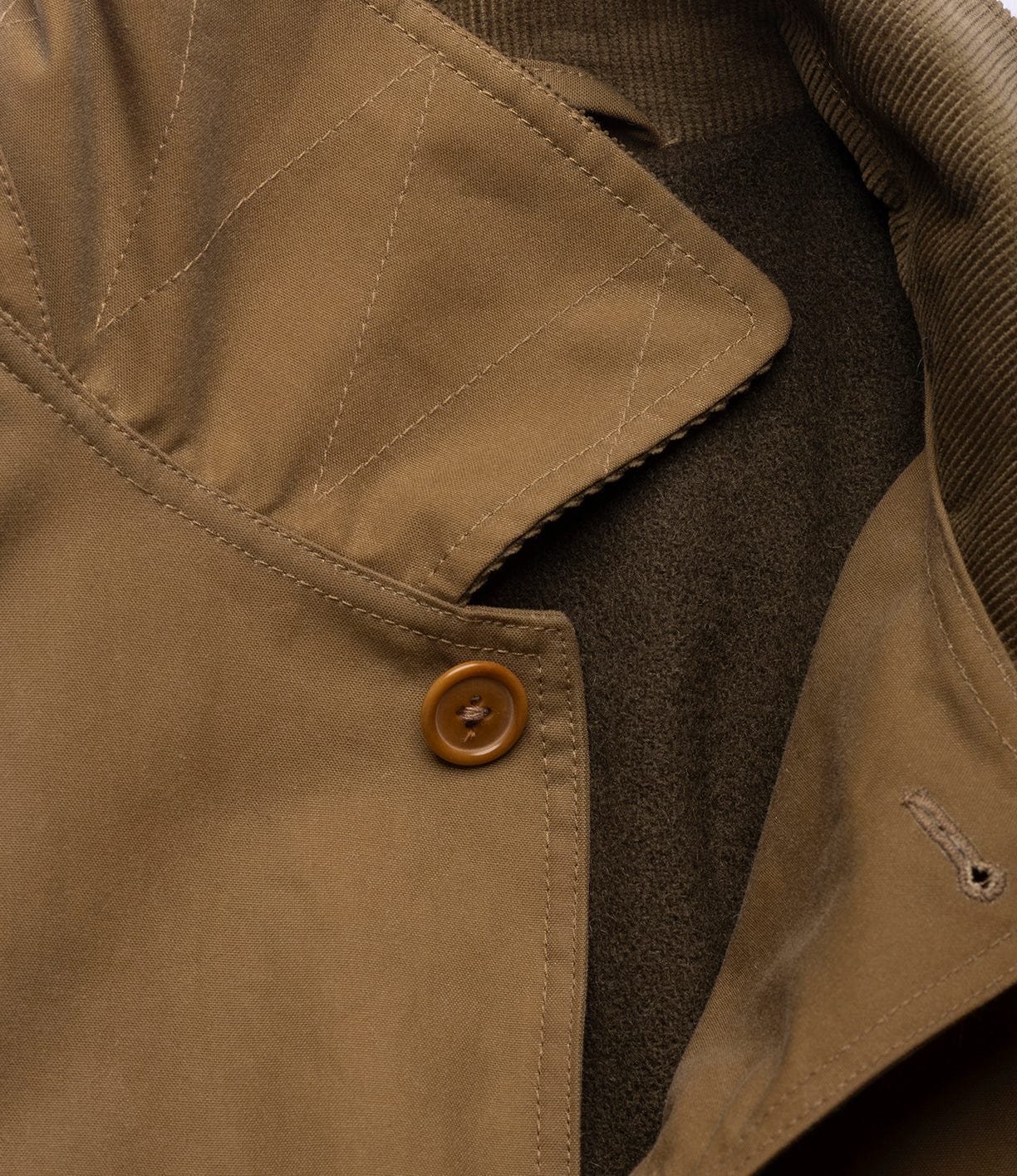 Close-up of the Best Made Co. Wool-Lined Waxed Field Jacket in tan, featuring a brown button, visible stitching, part of the collar, and layered fabric textures.
