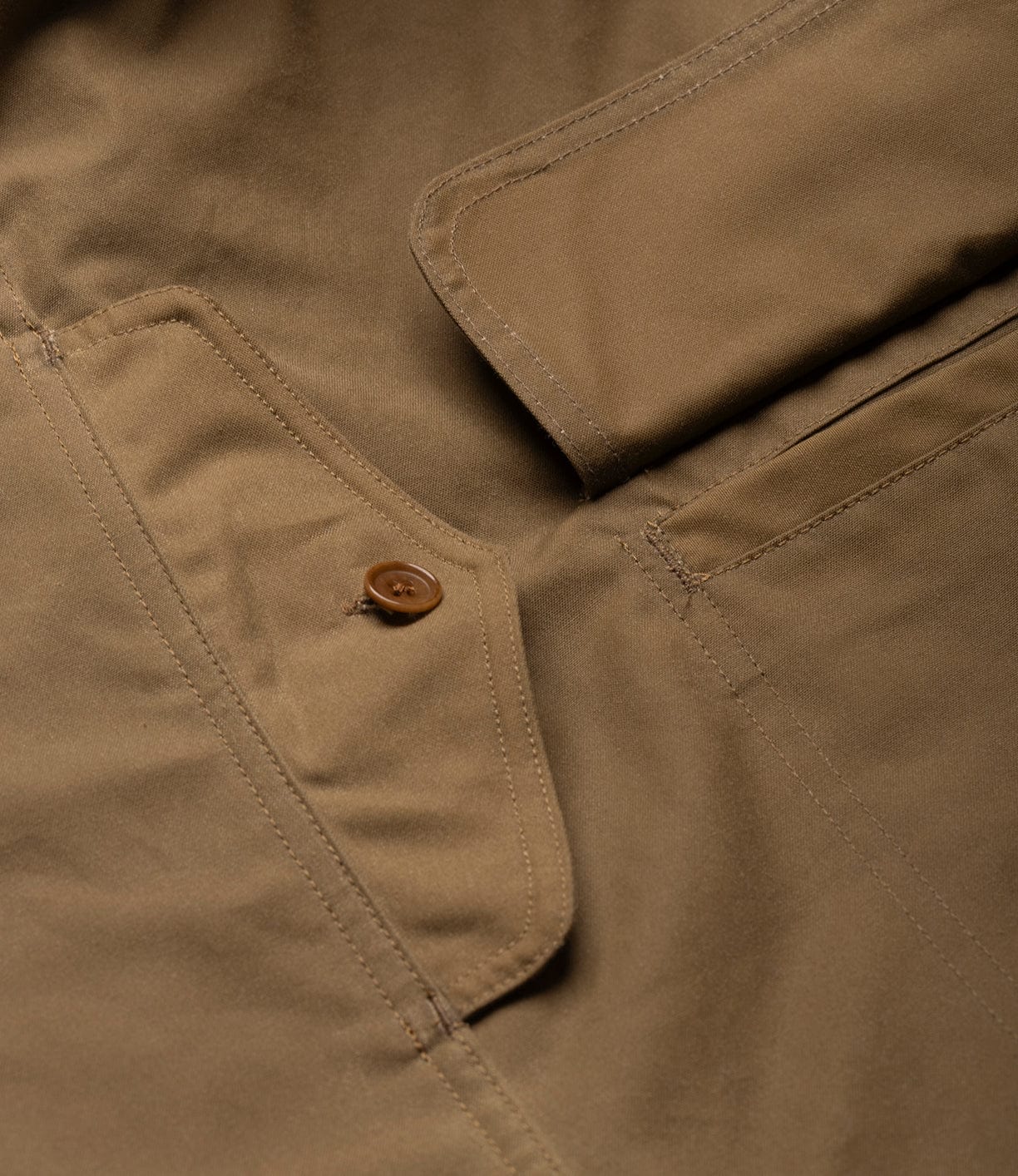 Close-up of the Best Made Co. Wool-Lined Waxed Field Jacket Tan highlighting detailed stitching, a buttoned flap pocket, and visible seam lines on smooth, matte, weather-resistant cotton.