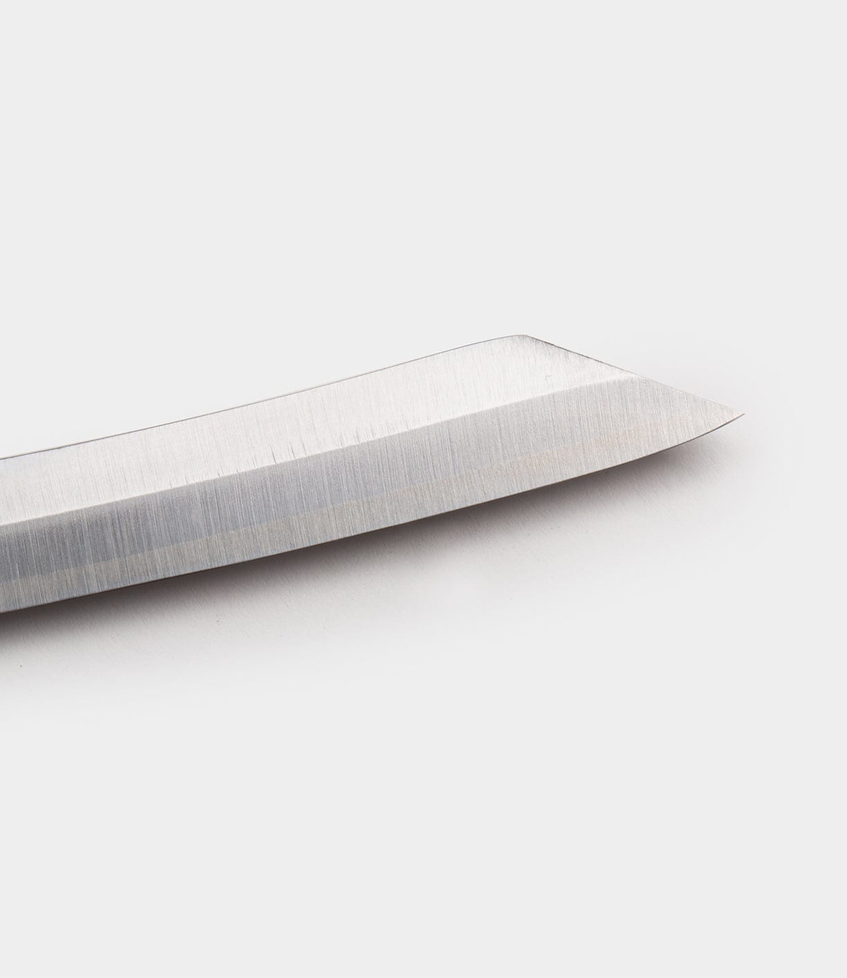 Close-up of the tip of a shiny, silver Max Brass Higo Knife by Best Made Co, set against a plain white background.