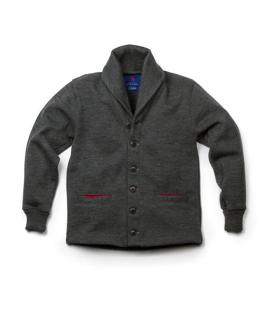 The Best Made Co. Dehen Shawl Neck Sweater Charcoal features a shawl collar, long sleeves, and two front pockets lined with red accents. The rugged sweater is displayed flat on a white background.