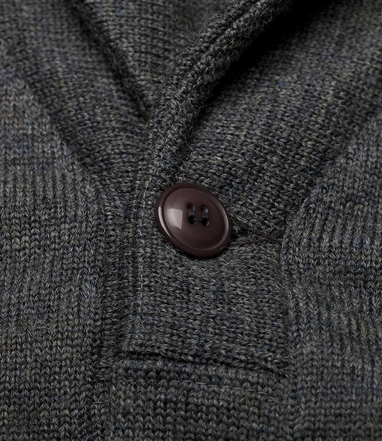 Close-up of the Dehen Shawl Neck Sweater Charcoal by Best Made Co., showing detailed grey knit texture and black button near the seam—exemplifying classic craftsmanship.