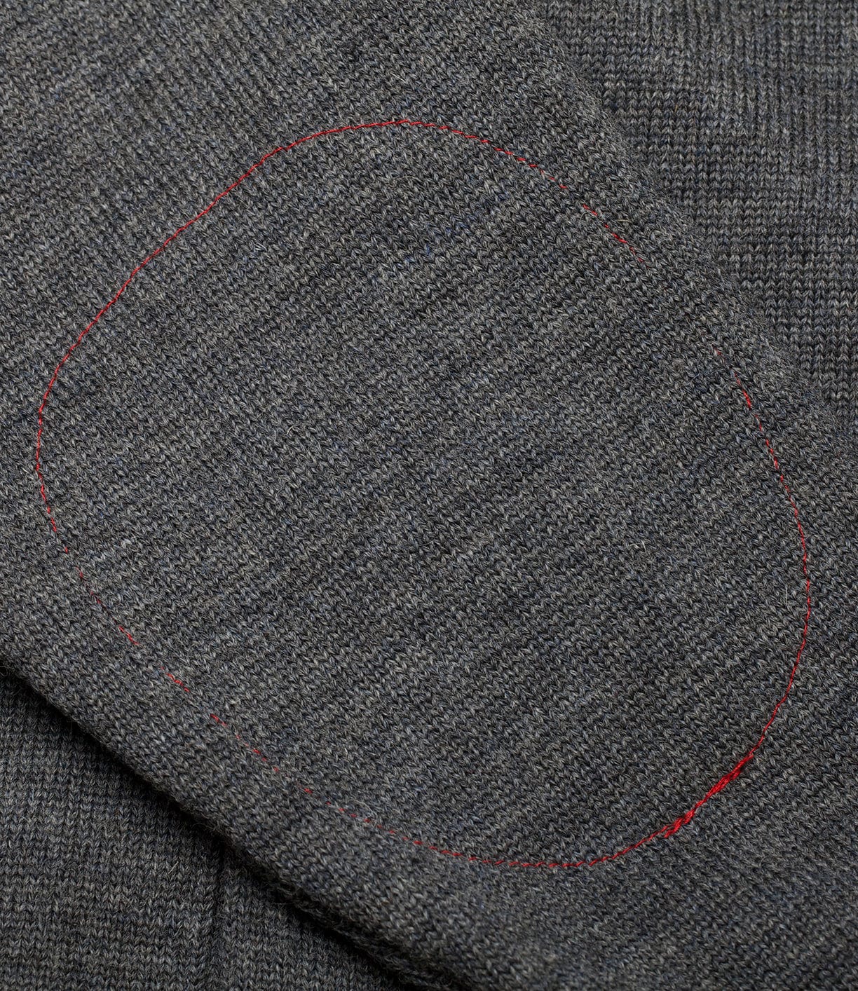 Close-up of the Dehen Shawl Neck Sweater Charcoal by Best Made Co., featuring gray knit fabric with an oval patch stitched in red thread, evoking classic Portland, Oregon sweater style.