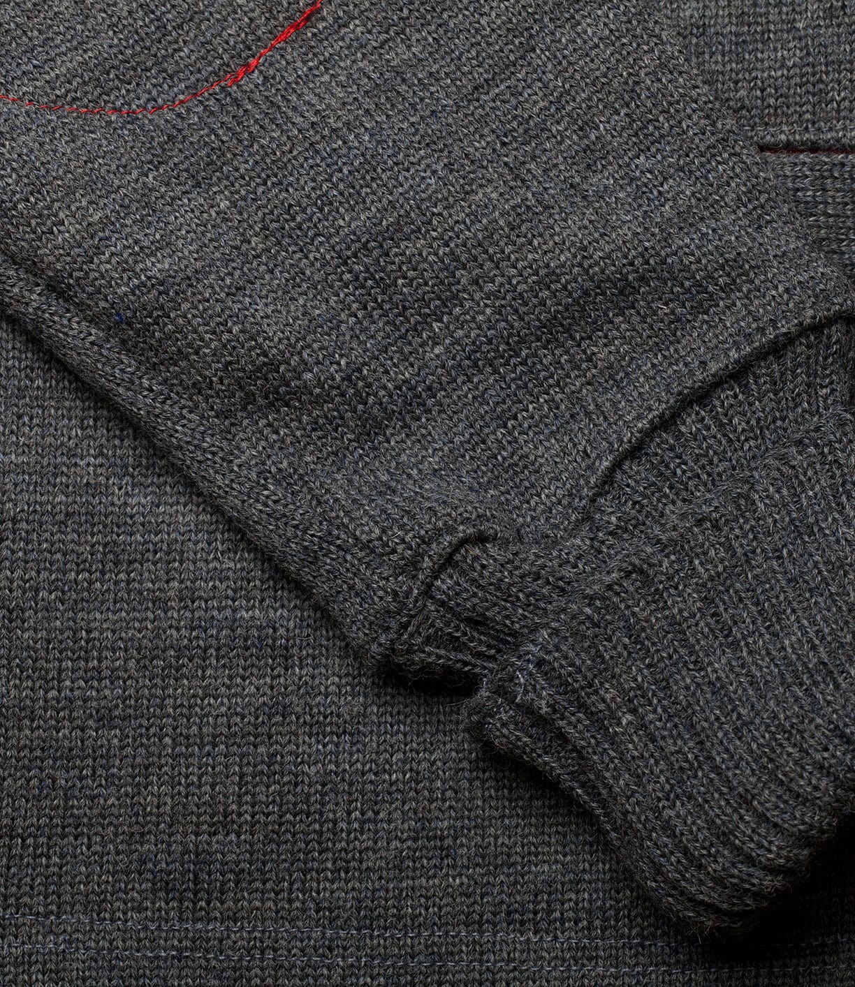 A close-up of the Best Made Co. Dehen Shawl Neck Sweater Charcoal sleeve laid across the body, featuring a red stitch near the top—a rugged sweater crafted in Portland, Oregon.