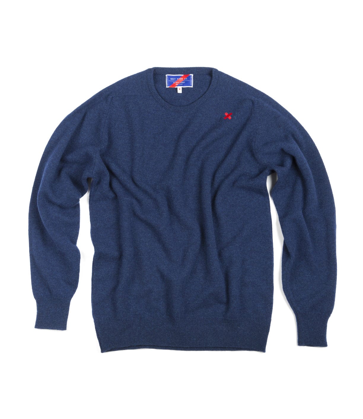 The Lightweight Shetland Sweater by Best Made Co. features blue lambswool, a crew neck, long sleeves, a small red embroidered left chest logo, and a visible neck tag, crafted in the tradition of Scottish woolen mills.
