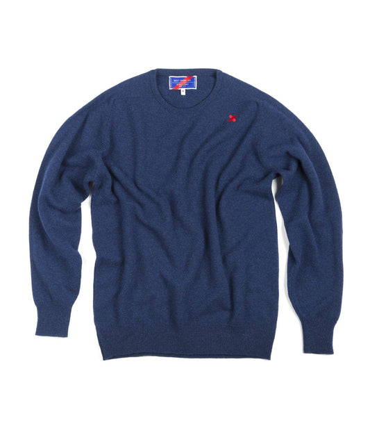 The Lightweight Shetland Sweater by Best Made Co. features blue lambswool, a crew neck, long sleeves, a small red embroidered left chest logo, and a visible neck tag, crafted in the tradition of Scottish woolen mills.