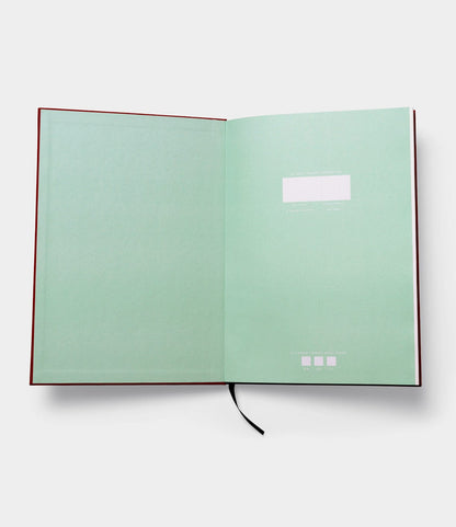 The Best Made Co. S.B.T. Max Cloth-Bound Notebook opens flat with mint green endpapers, a black ribbon bookmark, white label on the right page, subtle text at the bottom, and numbered pages for organized note-taking.
